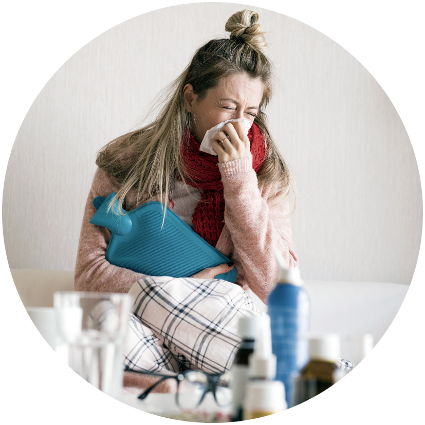 Image of female sneezing and holding a hot water bottle. 